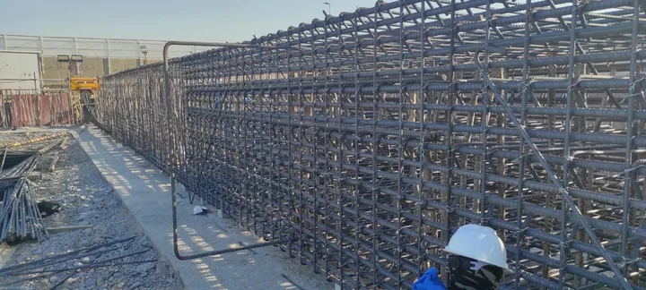 A worker beside a long multilayer steel reinforcement cage.