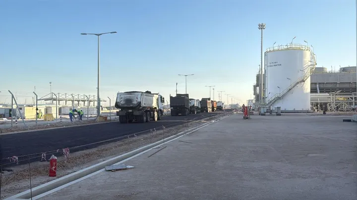 A roadway alongside storage tanks and industrial structures with work vehicles.