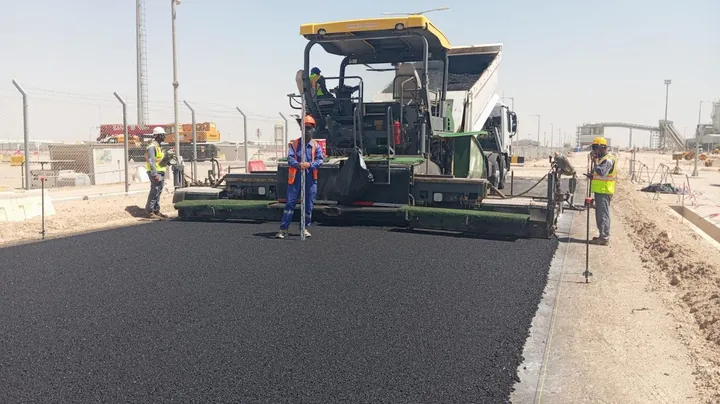 An asphalt paver and crew laying a black surface layer.