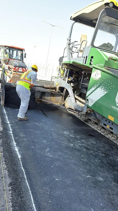 A worker beside an asphalt paver during road surfacing.