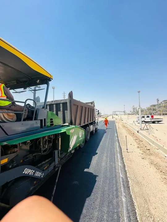 An asphalt paver beside a truck along the road.