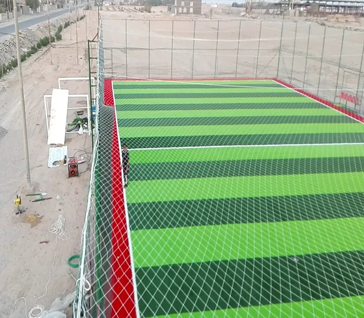 A rectangular striped artificial-turf pitch enclosed by fencing and netting.