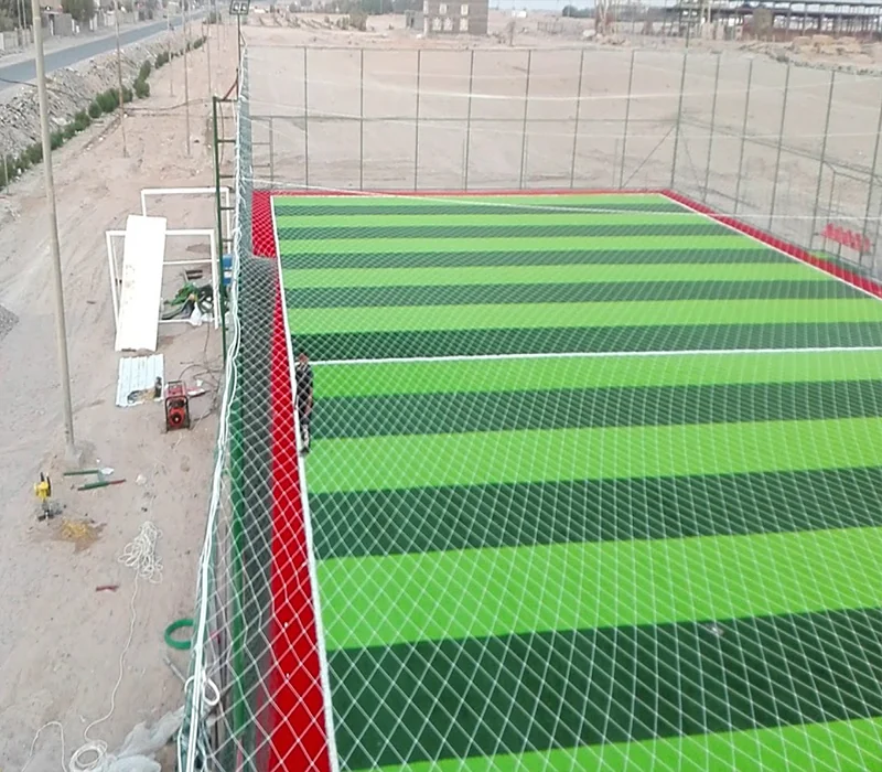 ملعب مستطيل بعشب صناعي مخطط محاط بشباك وسياج.